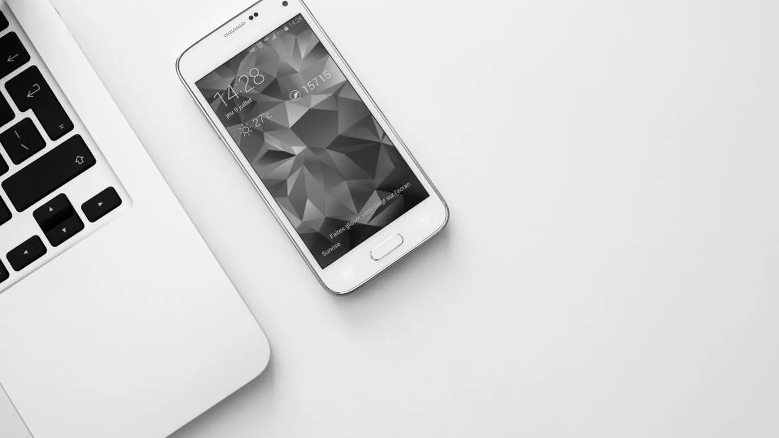 Smartphone next to a laptop on a white desk